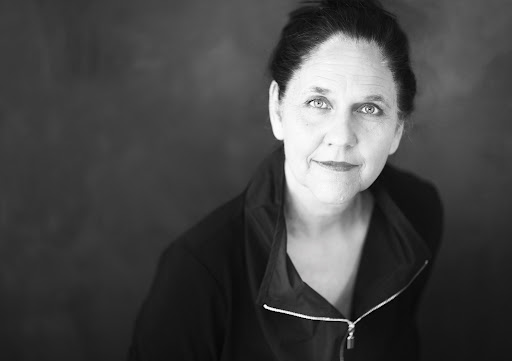 AI generated: The image shows a woman in a black and white portrait looking into the camera. The background is blurred and the focus is on her face and expression.